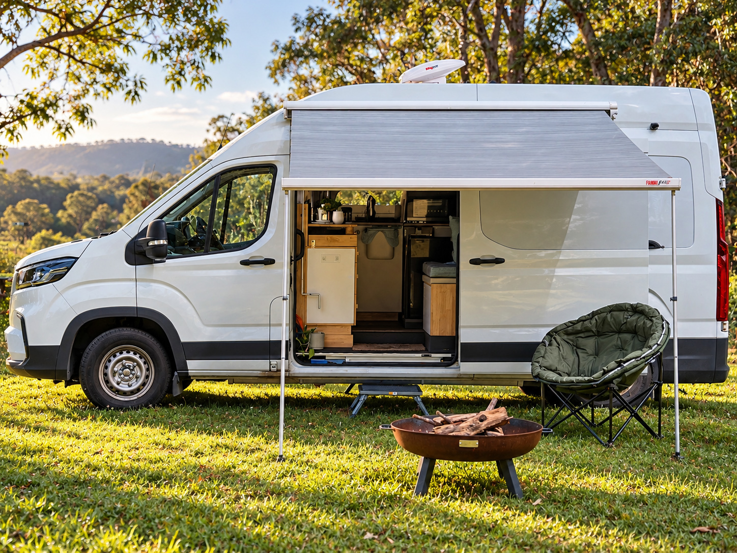 The campervan with its awning out, a fire pit and an outdoor chair on a grassy campsite